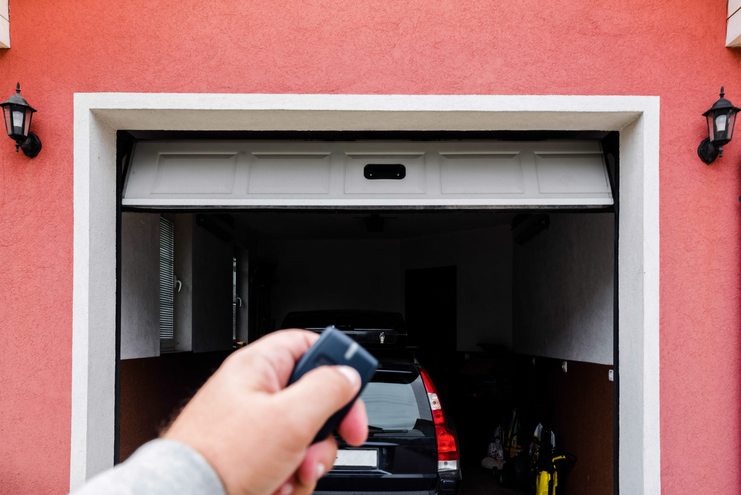 Hand pressing garage door opener in front of open garage door